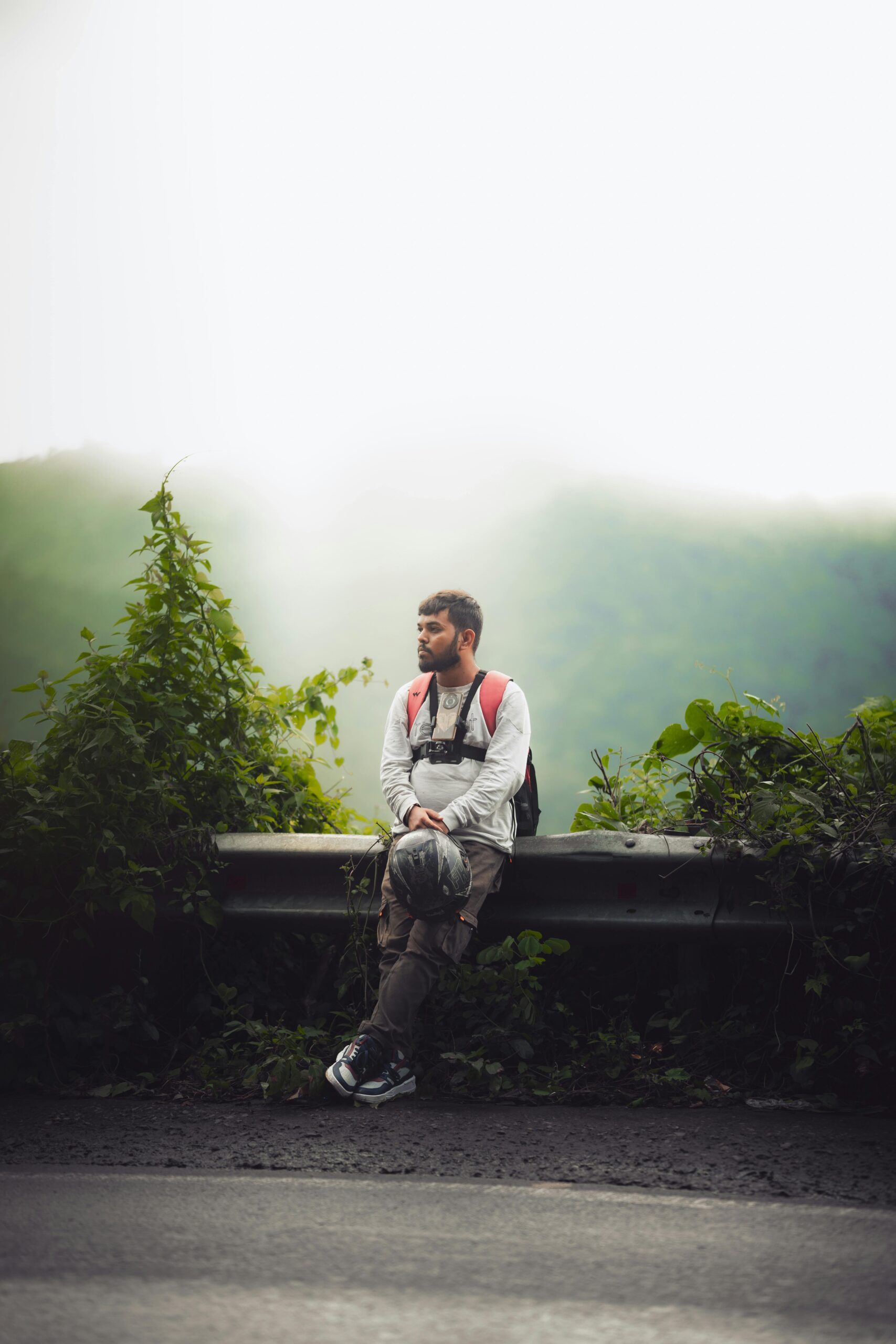 A man with a backpack enjoying a moment of rest by a misty mountain roadside in Chhattisgarh, India.