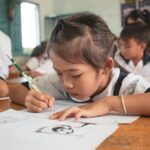 Child attentively drawing in a classroom setting. Education and creativity emphasized.