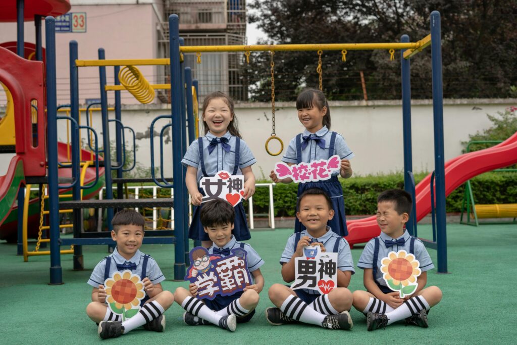 Smiling children in school uniforms holding signs at a vibrant playground on a sunny day.