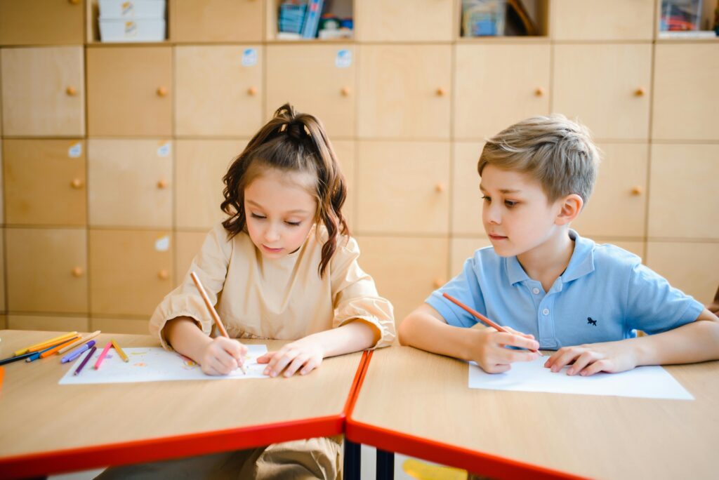 Kids drawing with colored pencils in a classroom setting, focused on creativity.