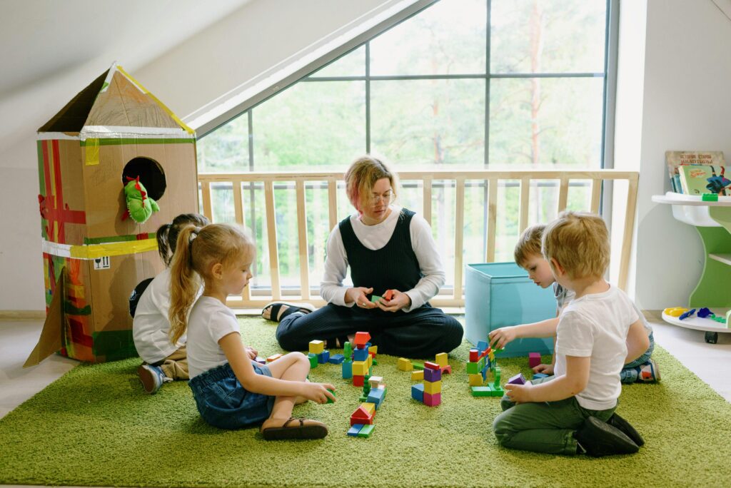 Children enjoying playtime with blocks and cardboard house in a cozy classroom.