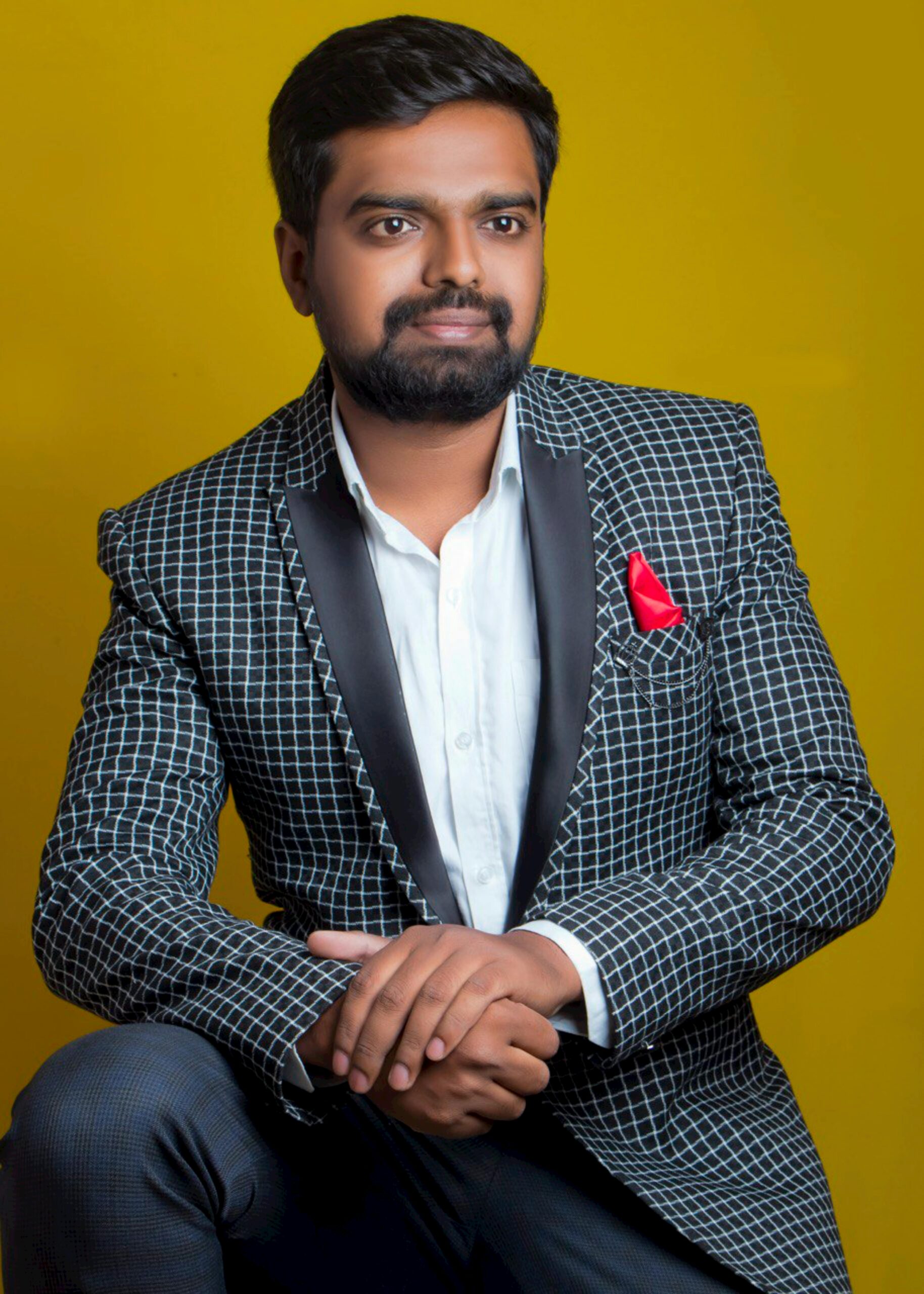 Studio portrait of a confident South Asian man in a stylish suit against a yellow backdrop.